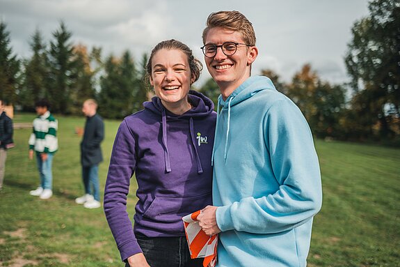zwei junge Menschen auf einem Feld lachen in die Kamera