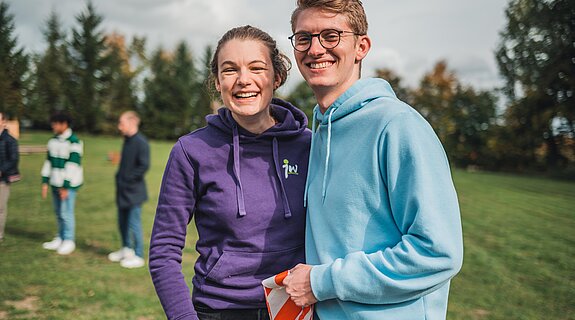 zwei junge Menschen auf einem Feld lachen in die Kamera