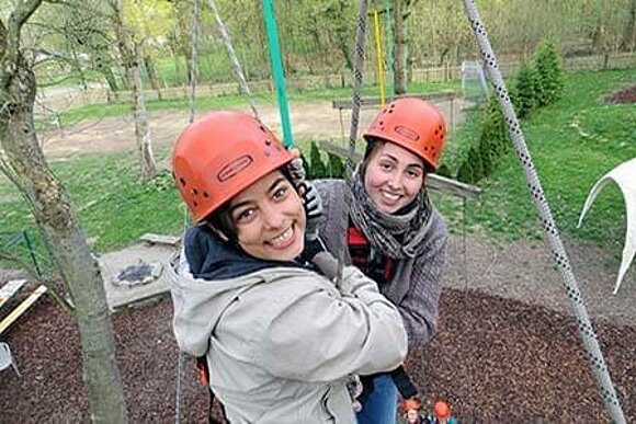 Zwei Frauen hängen an Seilen im Hochseilgarten