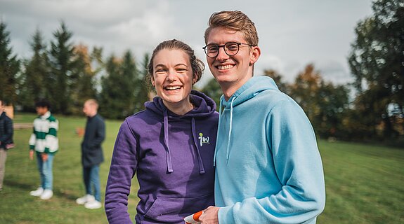 zwei junge Menschen auf einem Feld lachen in die Kamera