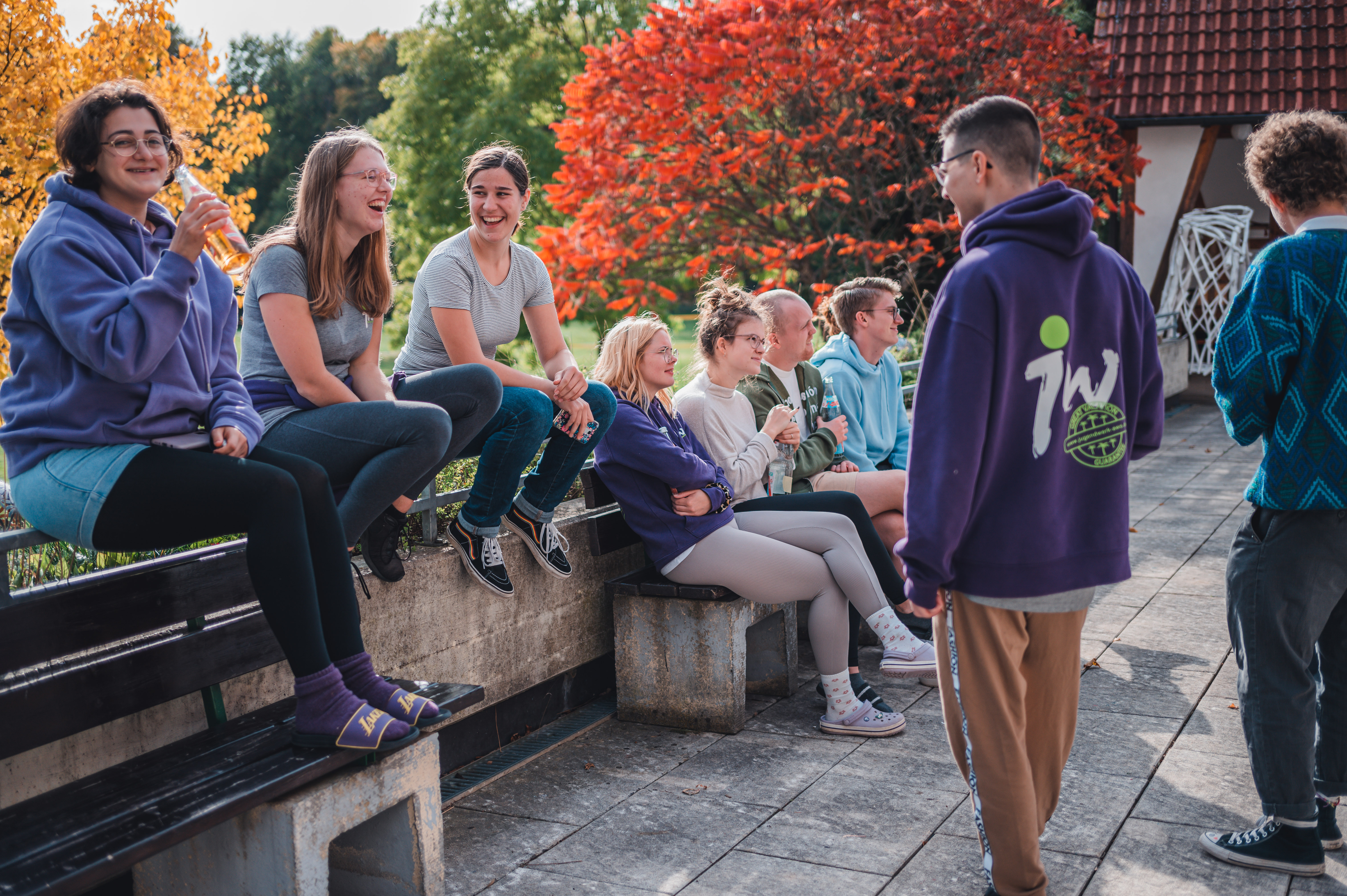 junge Menschen sitzen zusammen draußen im Hintergund bunte Bäume
